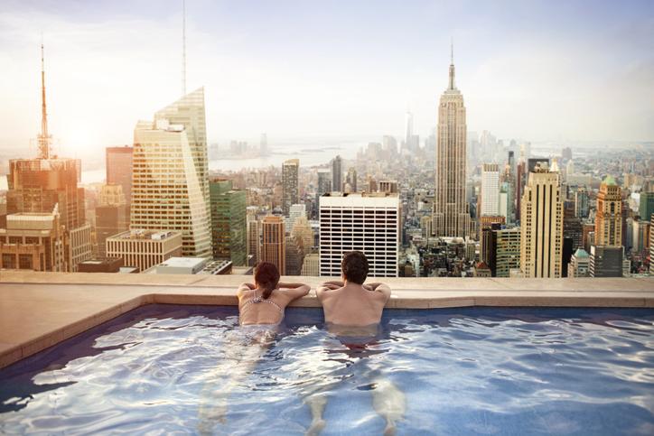Couple relaxing in swimming pool on hotel rooftop, overlooking impressive New York skyline.